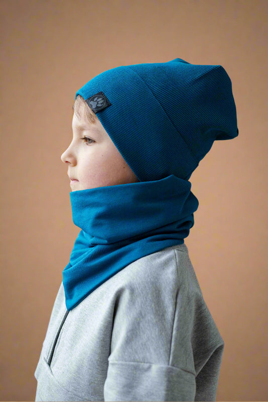 Child wearing a blue beanie and scarf against a brick wall